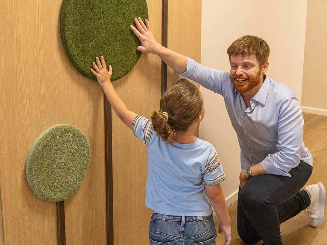 Dr. Murari agachado, sorrindo, brincando com uma criança em um painel sensorial